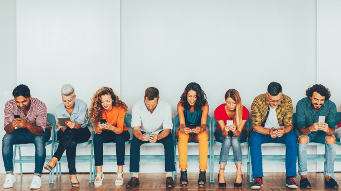 Multiple people sitting across a bench looking at their social media accounts on cell phones.